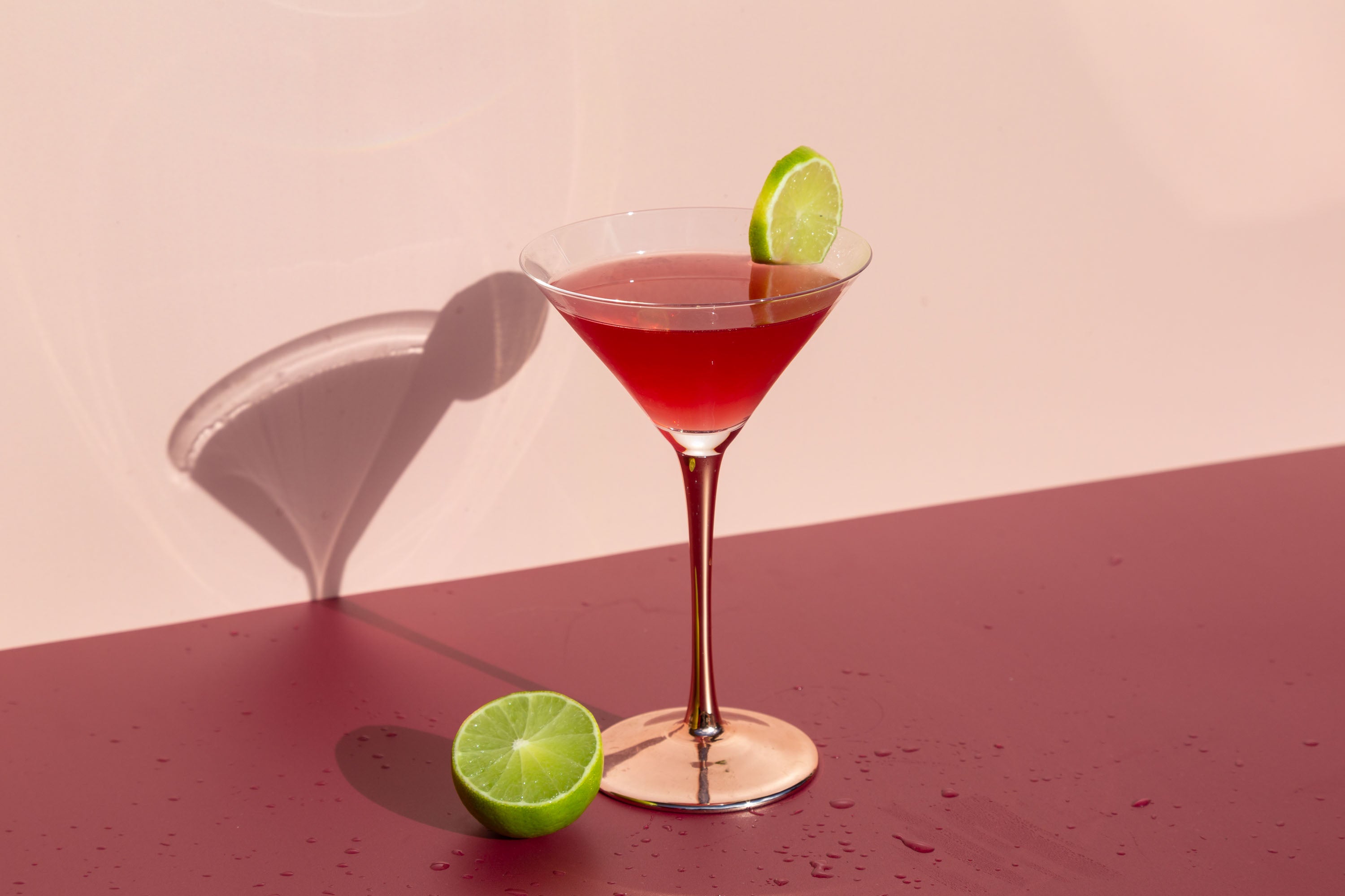 Cosmopolitan cocktail against pink backdrop with wedge of lime in foreground
