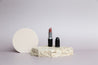mac lipstick photographed with small neutral acrylic circle and travertine stone on a taupe vinyl photography backdrop - backdrop collective australia