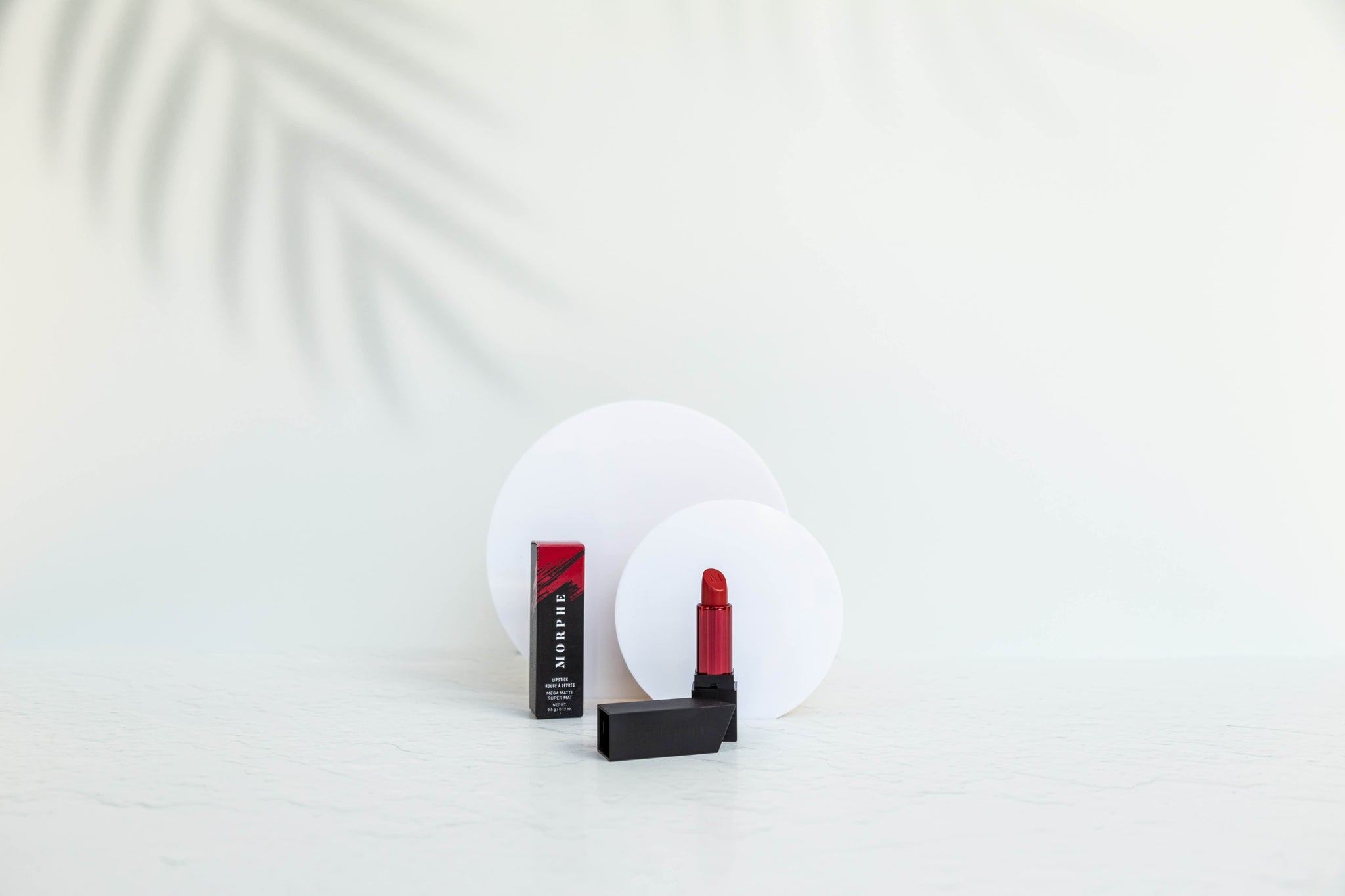 white palm tree leaf shadow photography backdrop and white acrylic circle photography props photographing red morphe lipstick for cosmetic product photography - backdrop collective australia